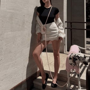 Woman in black top and white shorts standing next to a Dalmatian dog in a pink outfit against a concrete wall with the marshmallow hands-free lead across her body.