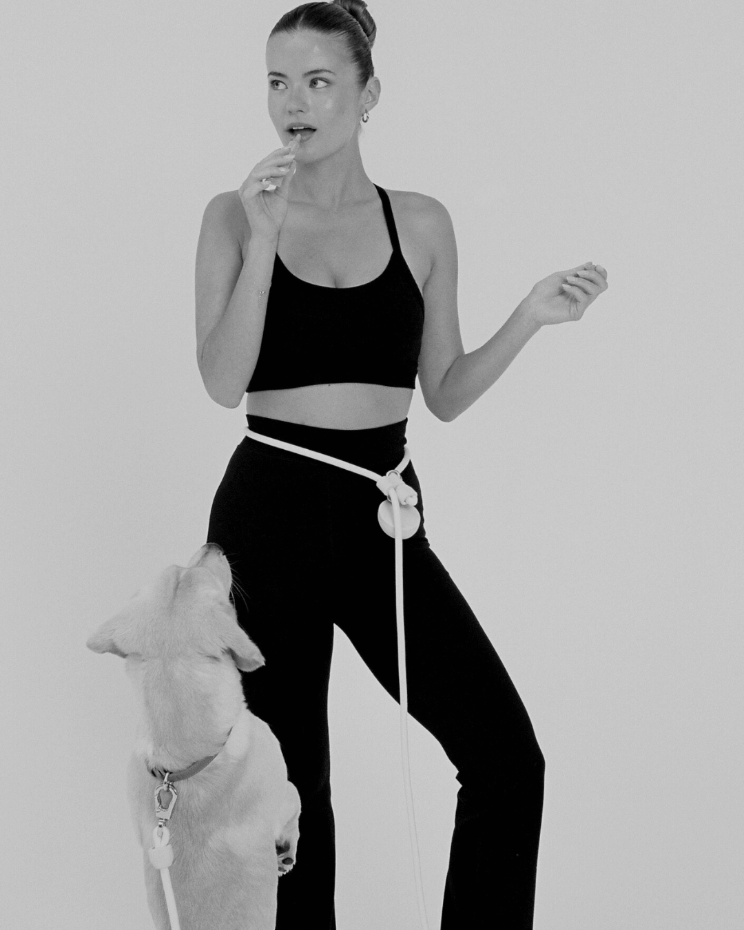 Woman in athletic wear standing next to a dog on a leash against a plain background